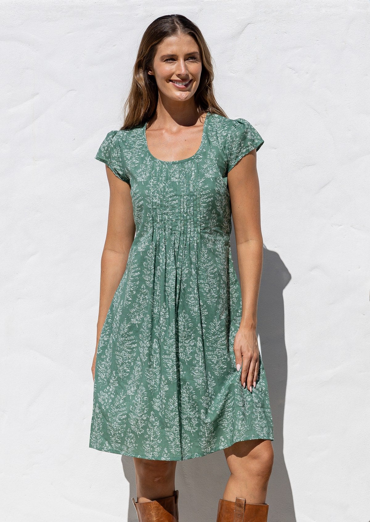 Woman wearing a 100% cotton sage green based floral dress with round neckline and cap sleeves.