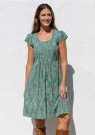 Woman wearing a 100% cotton sage green based floral dress with round neckline and cap sleeves.