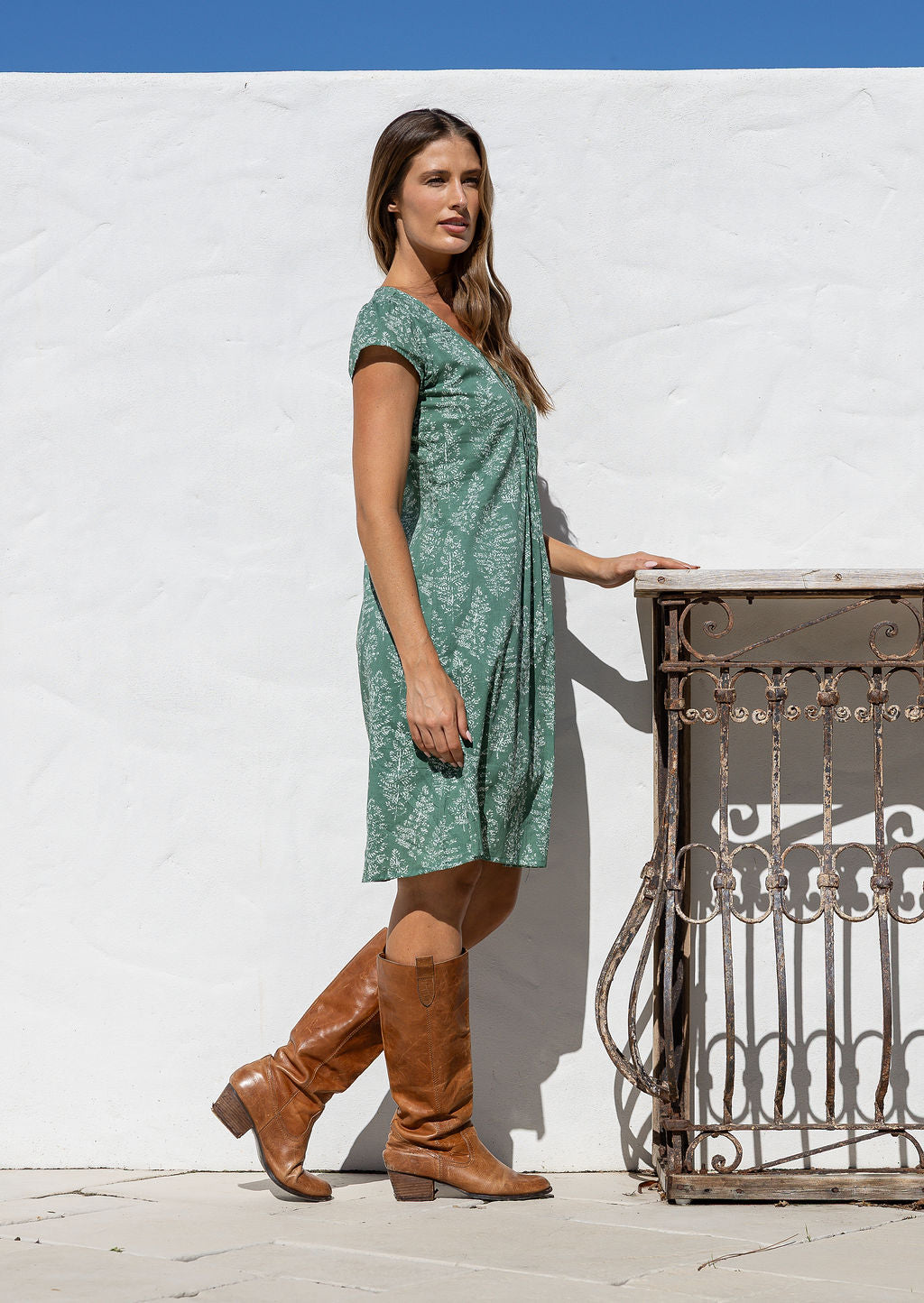 Woman stands sideways wearing a 100% cotton sage green based floral dress with round neckline.