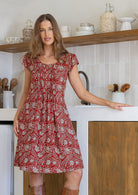 Woman standing wearing a 100% cotton red based floral dress with round neckline.