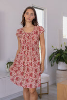 Woman wearing a 100% cotton floral dress in a bright room with white walls and a plant.