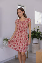 Woman wearing a 100% cotton gentle cream based floral dress in a modern room with white walls and plants.