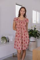 Woman wearing a 100% cotton gentle cream based floral dress with round neckline and cap sleeves.