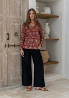 Model wearing a flattering long sleeve top with beautiful red based florals with plain black pants.