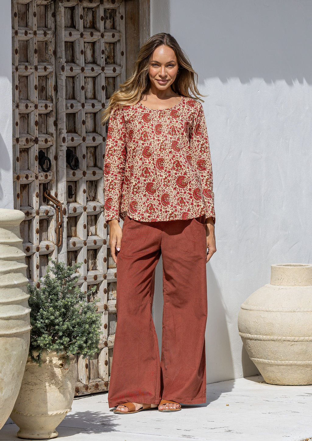 Model wearing 100% cotton long sleeve top with round neckline and tiny pleat detail from the center of the neckline.