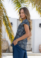 Woman stands sideways wearing  100% cotton top in navy blue based floral print with navy plain pants. 