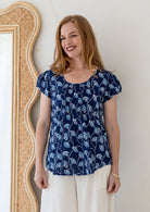 Woman wears navy based floral print 100% cotton cap sleeve top with pin tuck detail across the bust and a scoop neckline