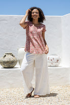 Woman wears rose pink based floral print 100% cotton cap sleeve top with pin tuck detail across the bust and a scoop neckline
