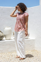 Woman standing sideways wears 100 percent cotton top with short cap sleeves and longer back hem.