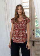 Woman wears red based floral print 100% cotton cap sleeve top with pin tuck detail across the bust and a scoop neckline