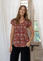 Woman wearing a red based floral print short sleeve top with scoop round neckline and pleated detail across the bodice