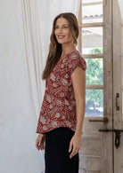 Woman stands sideways wearing  100% cotton top in red based floral print.