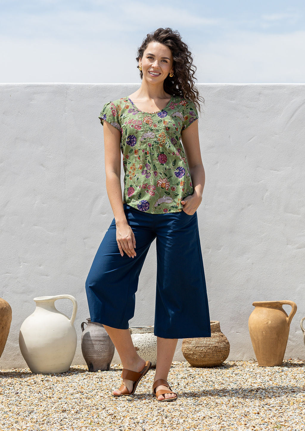 Woman wearing a moss green based floral  print short sleeve top with scoop round neckline and pleated detail across the bodice