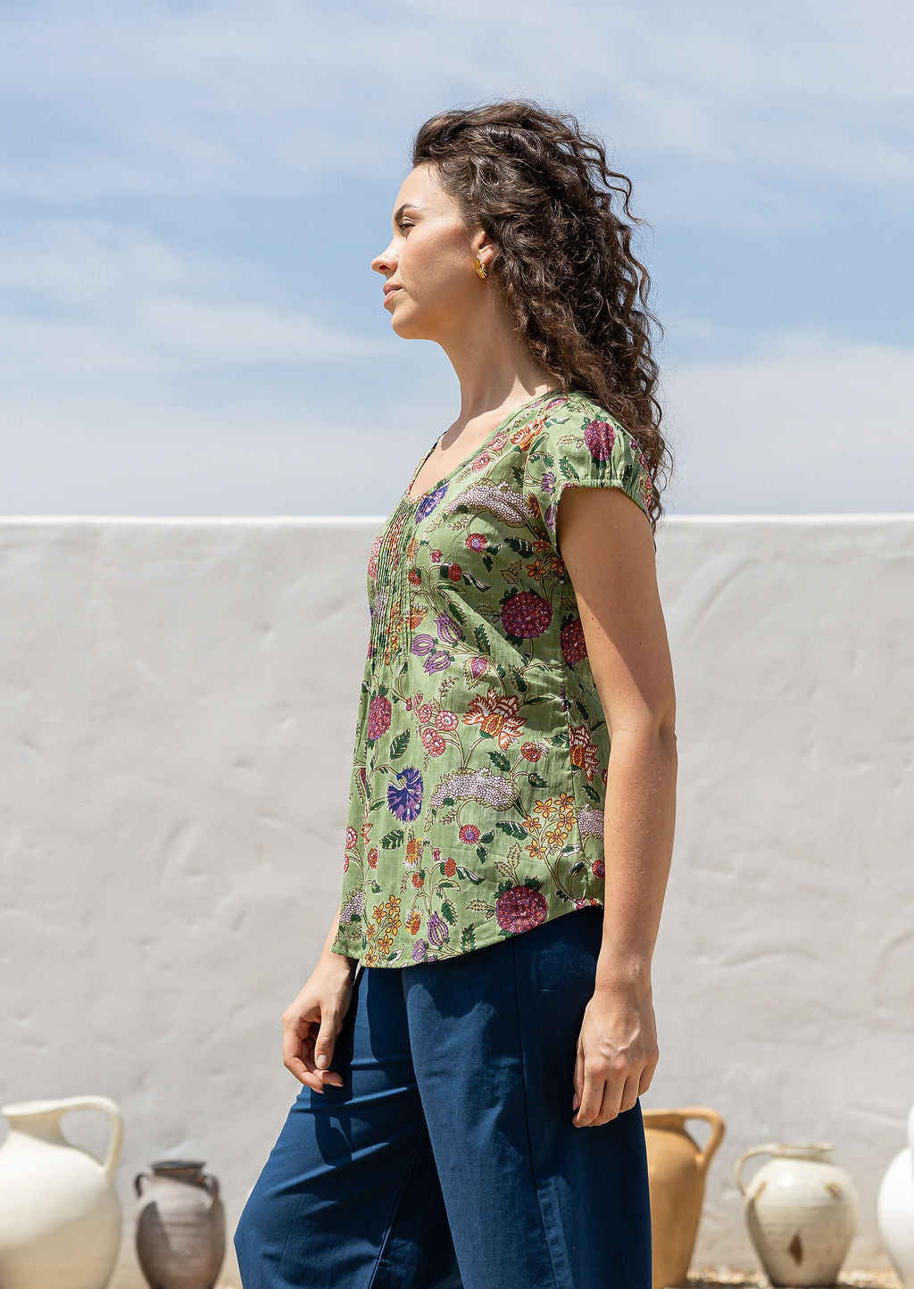 Woman standing sideways wears 100 percent cotton top with short cap sleeves and longer back hem.