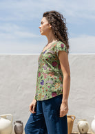 Woman standing sideways wears 100 percent cotton top with short cap sleeves and longer back hem.