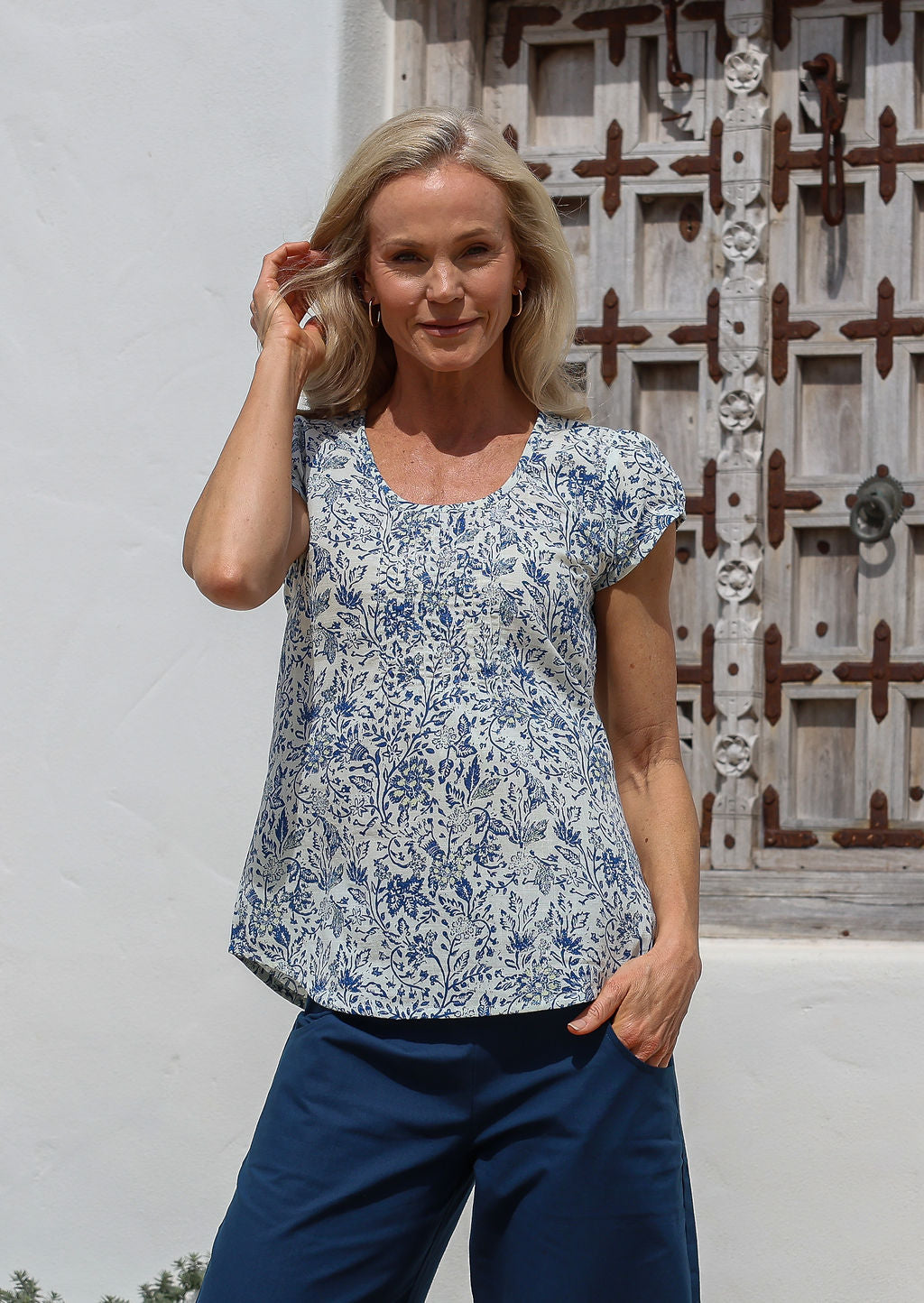 Woman wears a white based floral cotton cap sleeve top with pin tuck detail across the bust and a scoop neckline