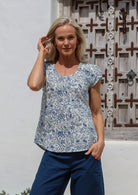 Woman wears a white based floral cotton cap sleeve top with pin tuck detail across the bust and a scoop neckline