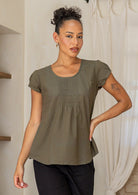 Woman wearing a green cotton short sleeve top with a scoop neckline and pin-tucks across the centre bodice paired with black pants