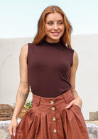 Woman standing side on wearing a sleeveless brown stretch rayon jersey top with a mock turtleneck, paired with skirt