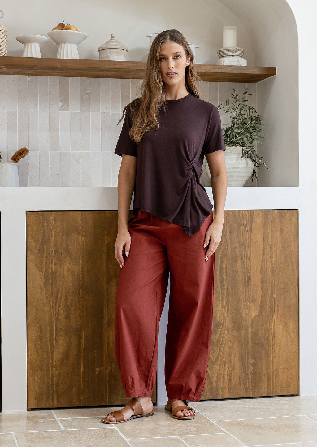 Woman wearing a relaxed fit short sleeve brown rayon jersey top with a twist detail in the front, paired with rust pants