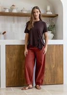 Woman wearing a relaxed fit short sleeve brown rayon jersey top with a twist detail in the front, paired with rust pants