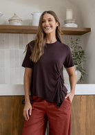 Woman smiling wearing a relaxed fit short sleeve brown rayon jersey top with a twist detail in the front and rust pants