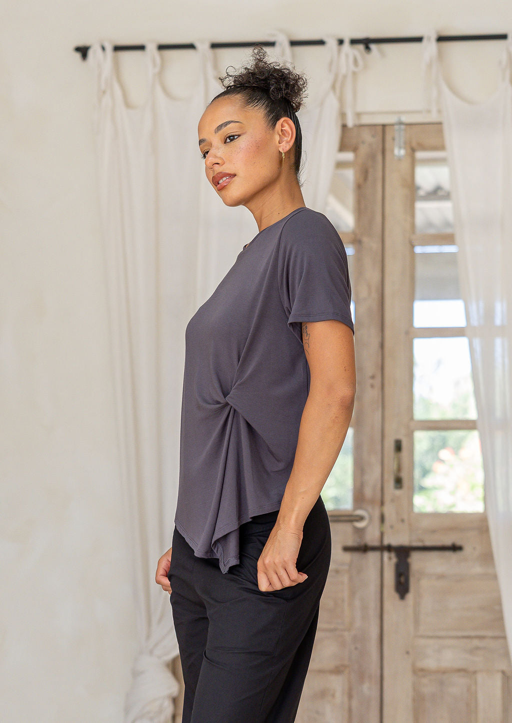 Woman wearing Dark grey women’s twist-front T-shirt, stretch rayon short-sleeve top with subtle draped knot in a home setting