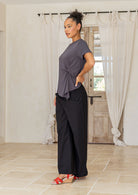 Woman wearing a gray top and black pants standing in a room with white curtains and a wooden door.