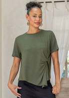 Woman wearing an olive green twist-front rayon T-shirt with short sleeves and a subtle draped knot at the front over black cotton pants