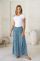 Woman wearing a white stretch top with 100% rayon wide legged flowy pants in blue based floral print with smocked elastic waistband.