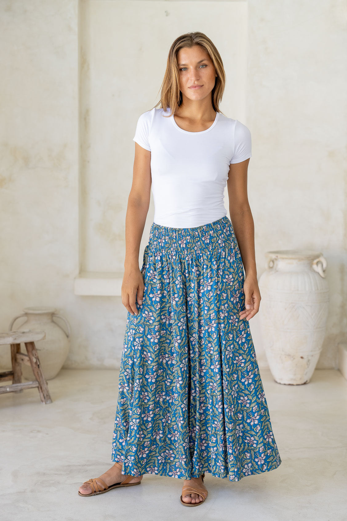 Woman wearing a basic white t-shirt and super wide leg blue floral pants in a bright room.