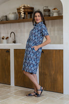 Woman standing sideways wearing a 100% cotton relaxed fit collared short sleeve dress with hidden side pockets. 