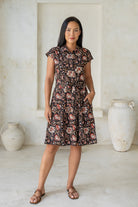 Model stands with one hand in pocket wearing a 100% cotton knee length shirt style retro floral dress in black based indian traditional print.