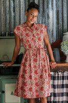 Model posing wears 100% cotton floral print shirt style dress with cap sleeves, fabric waist tie and box pleats at the waist.