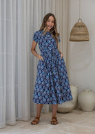 Woman wears retro style cotton button through midi length dress with high round neckline, short sleeves and a removable waist tie.