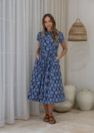 Woman wears 100% cotton button through midi length dress with short sleeves and pockets in floral print on a navy base