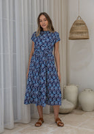 Woman in a floral dress standing in front of a white curtains.
