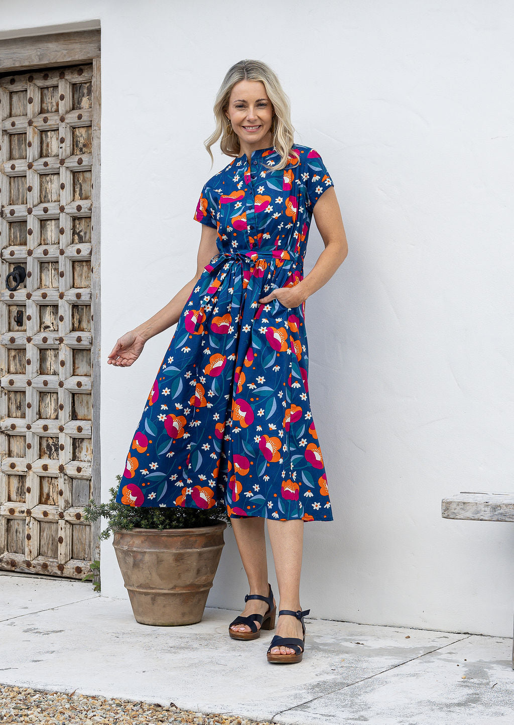 Woman wears retro style cotton button through midi length dress with high round neckline, short sleeves and a removable waist tie.