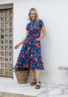 Woman wears retro style cotton button through midi length dress with high round neckline, short sleeves and a removable waist tie.