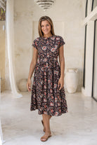 Woman wears 100% cotton button through midi length dress with short sleeves and pockets in indian floral print on a black base.