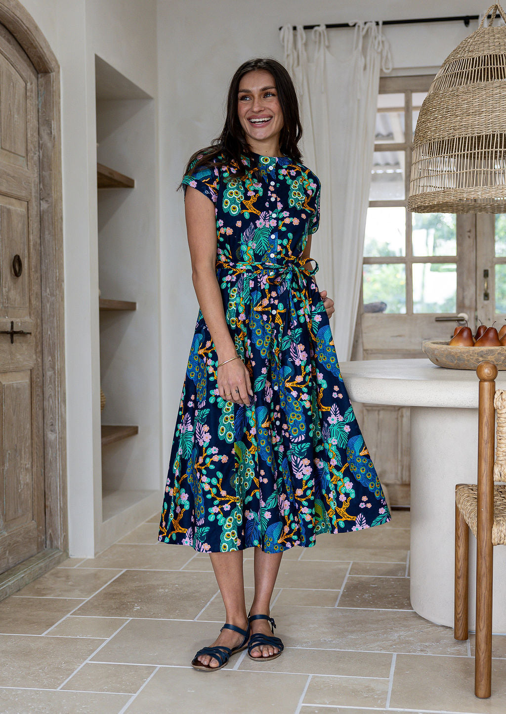 Woman wears 100% cotton button through midi length dress with short sleeves and pockets in floral print on a navy base