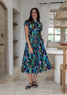 Woman wears 100% cotton button through midi length dress with short sleeves and pockets in floral print on a navy base