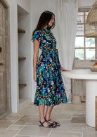 Woman standing sideways wearing a 1950's style short sleeved, button through cotton dress and high round neckline.
