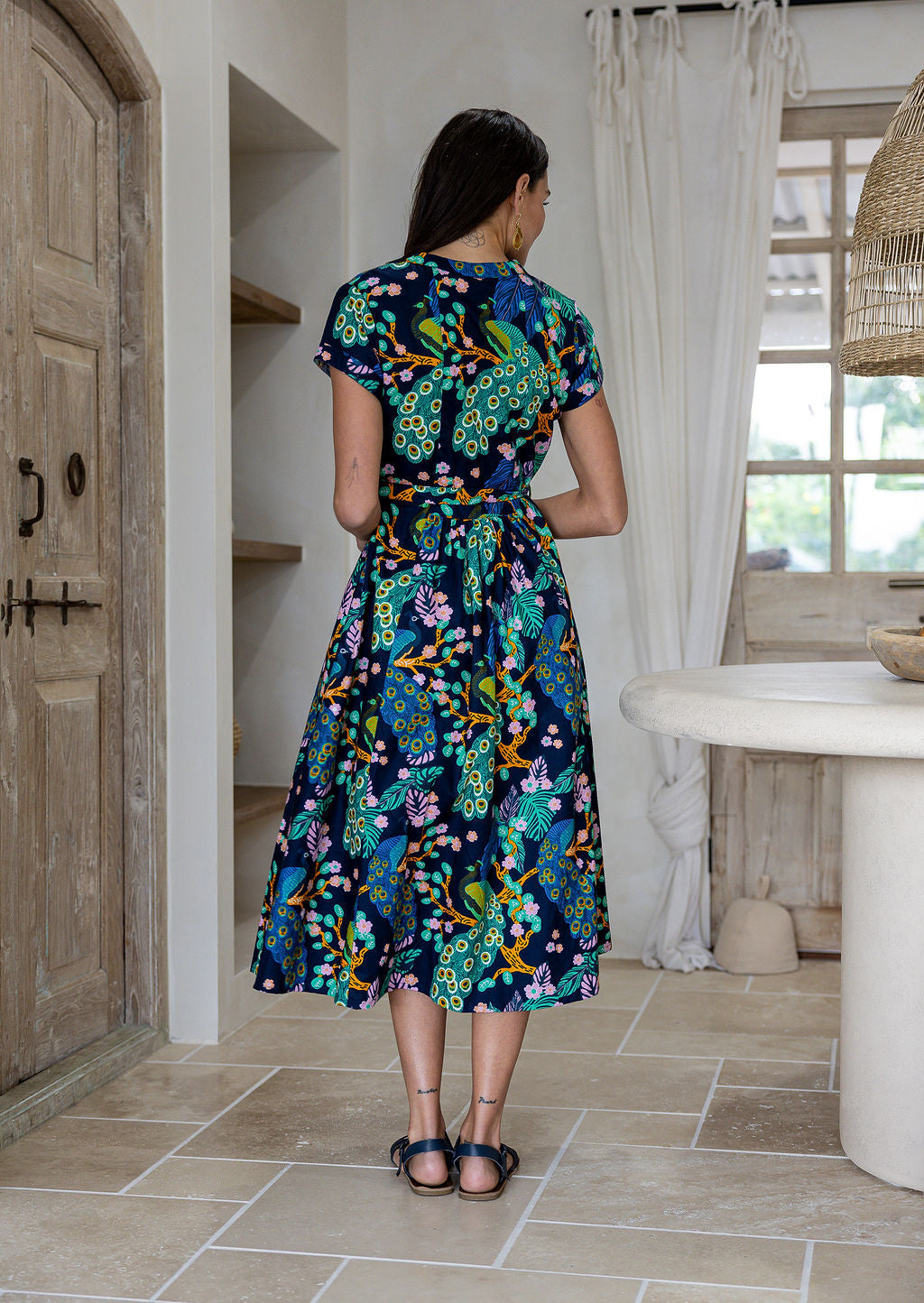 Woman standing backwards wearing a 1950's style short sleeved, button through cotton dress and high round neckline.