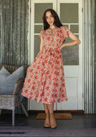 Woman wears retro style cotton button through midi length dress with high round neckline, short sleeves and a removable waist tie.