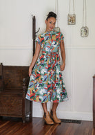 Woman wears retro style cotton button through midi length dress with high round neckline, short sleeves and a removable waist tie.
