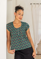 Woman wearing a green based floral print cotton top with dark pants.