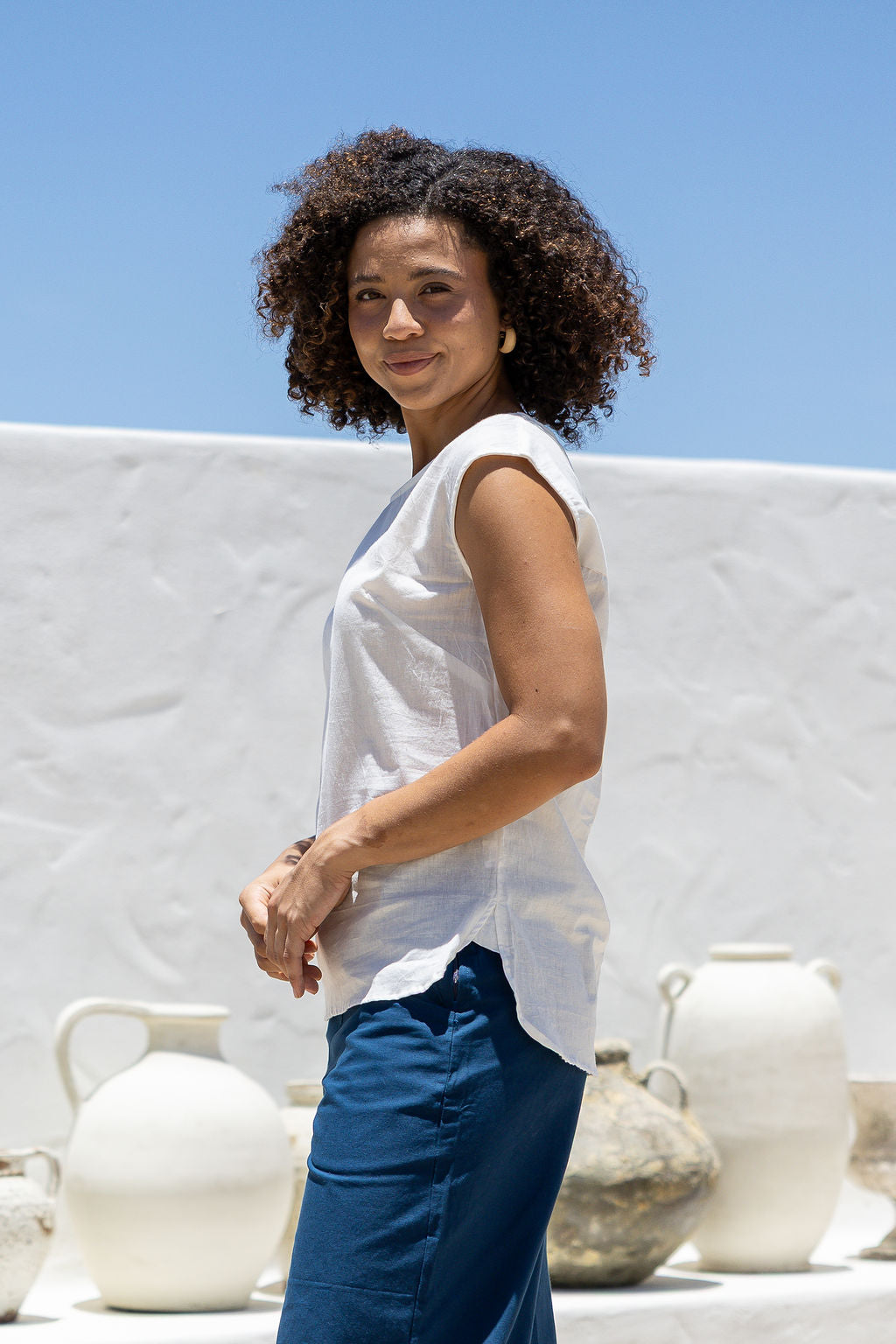 Woman in a white sleeveless cotton top that is longer at the back, paired with blue pants