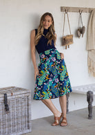Woman is posing with one hand in pocket wearing a 100% cotton navy based floral print a line skirt.