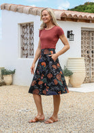 Woman is posing with one hand in pocket wearing a 100% cotton black a-line skirt with a moody botanical print 